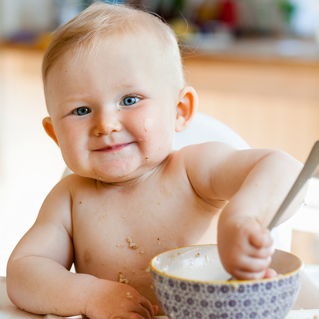 Smiling baby at table eating with spoon